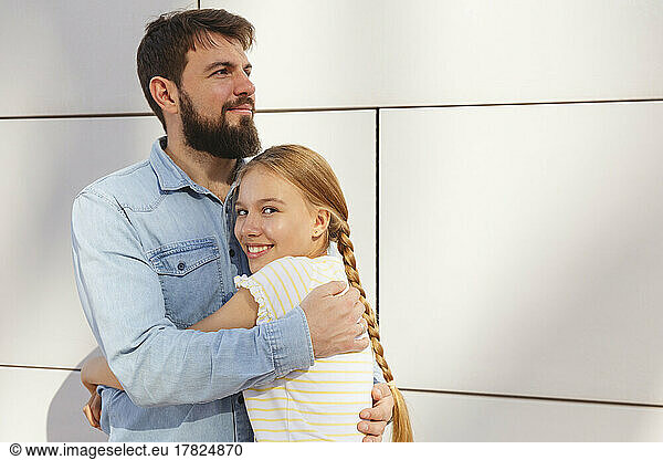 Happy girl embracing father in front of wall
