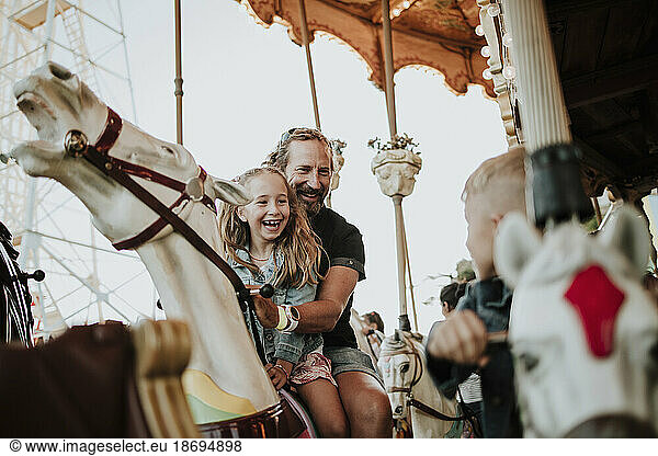 Happy girl enjoying carousel ride with father at amusement park