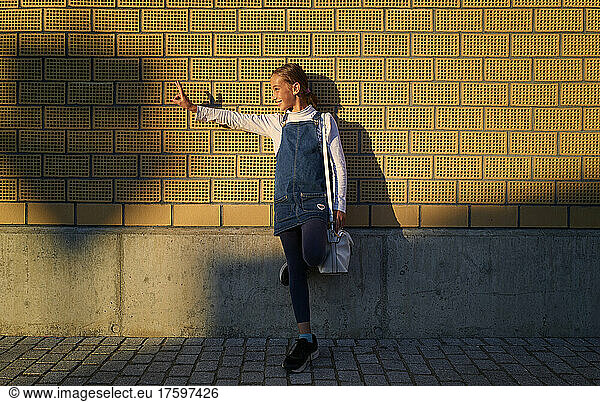 Happy girl gesturing peace sign standing on one leg in front of brick wall