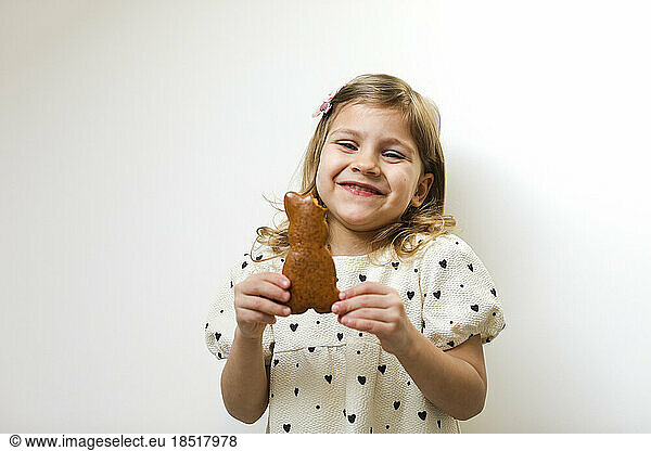 Happy girl holding bunny shape gingerbread against white background