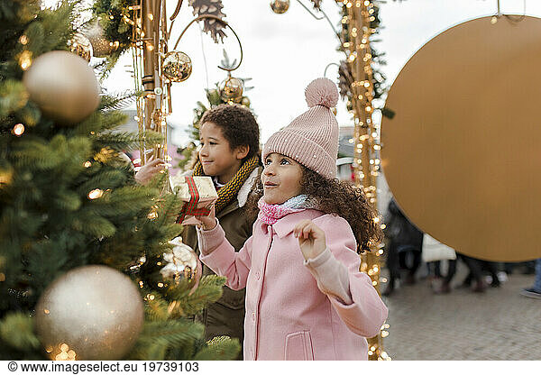 Happy girl holding gift box and enjoying with brother at Christmas market