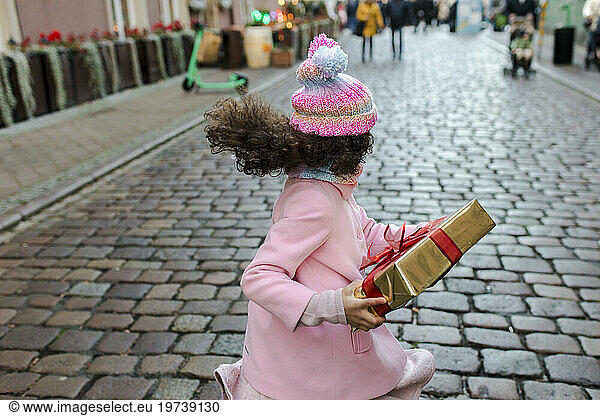 Happy girl holding gift box and running on street