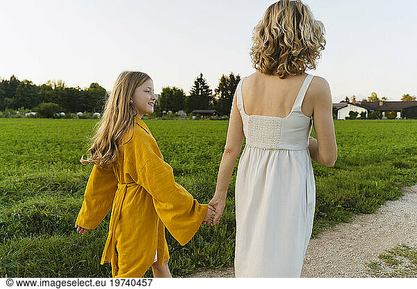 Happy girl holding hands with mother and walking on road