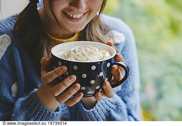 Happy girl holding mug of hot chocolate with whipped cream