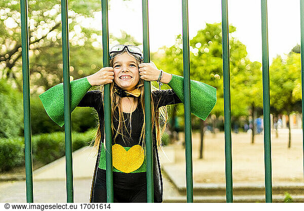Happy girl in super heroine costume behind bars