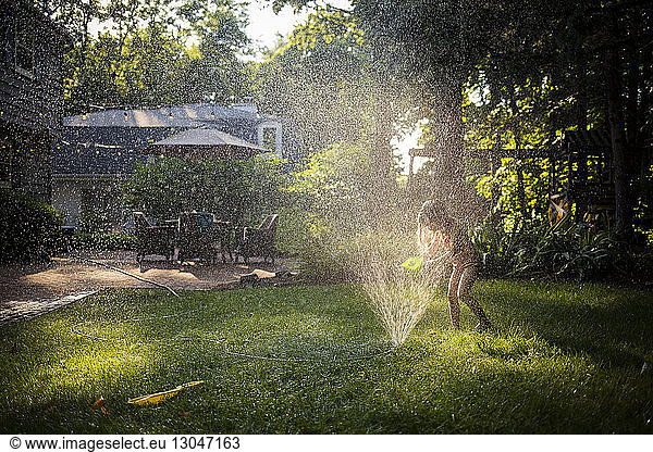 Happy girl in swimwear playing with sprinkler in backyard