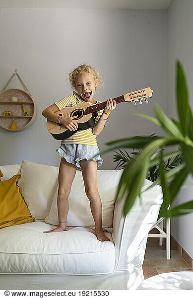 Happy girl playing guitar on couch in living room at home