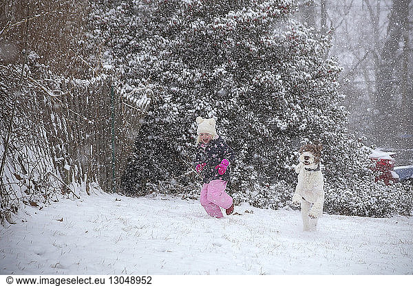 Happy girl playing with dog on field during snowfall