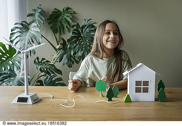 Happy girl playing with wind turbine and house model on table