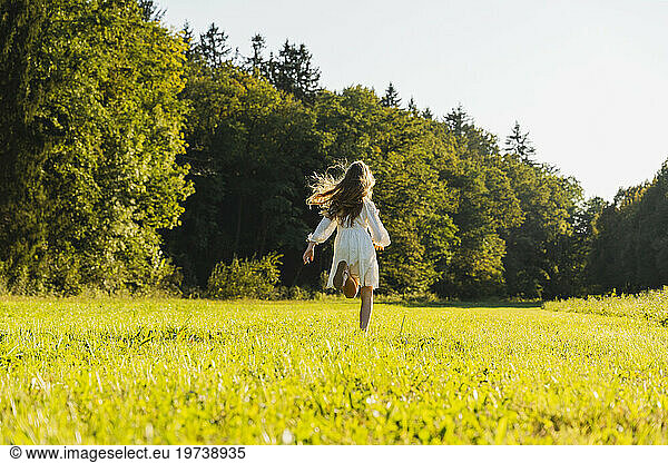 Happy girl running in front of trees in meadow