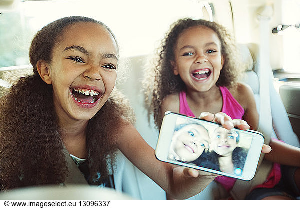 Happy girl showing photograph in smart phone while traveling with sister