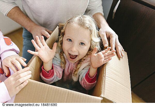 Happy girl sitting in cardboard box with sister and father at home