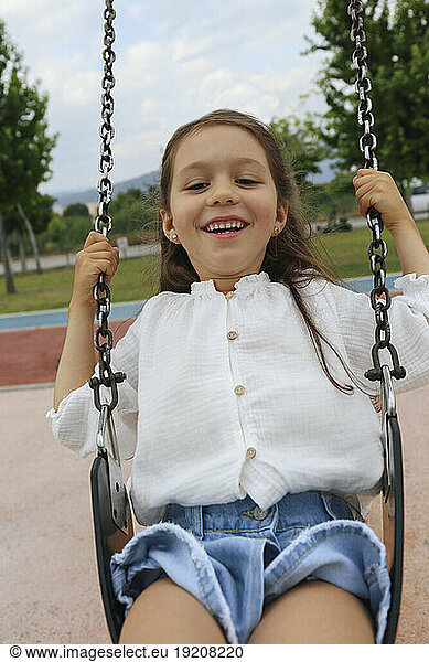 Happy girl sitting on swing at playground