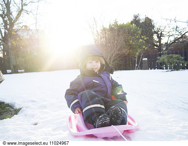 Happy girl sledding on snow covered field