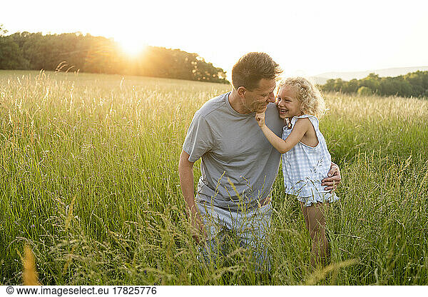 Happy girl standing by father kneeling on grass at field