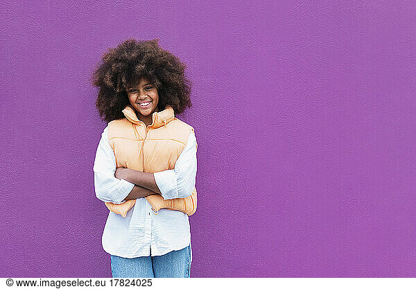 Happy girl standing with arms crossed against purple background