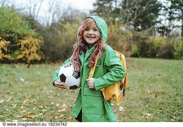 Happy girl standing with backpack and soccer ball at park