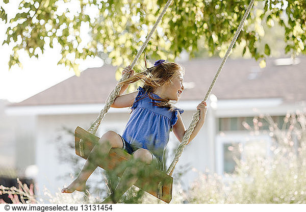 Happy girl swinging on rope swing at front yard
