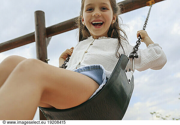 Happy girl swinging on swing under sky