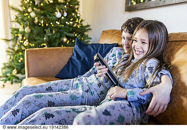 Happy girl watching TV with brother at home at Christmas time
