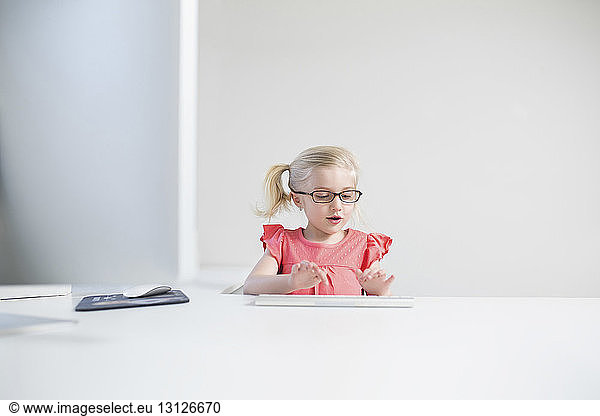 Happy girl wearing eyeglasses typing on keyboard at white table