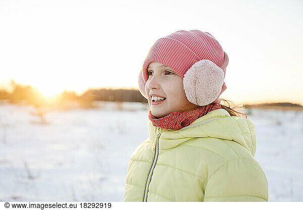 Happy girl wearing knit hat and ear muff in winter forest