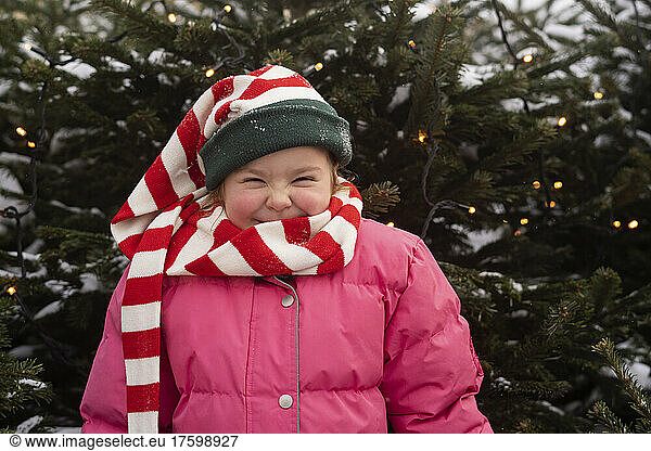 Happy girl wearing striped scarf standing in front of Christmas tree