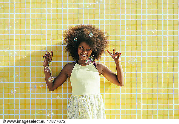 Happy girl with Afro hairstyle gesturing peace sign