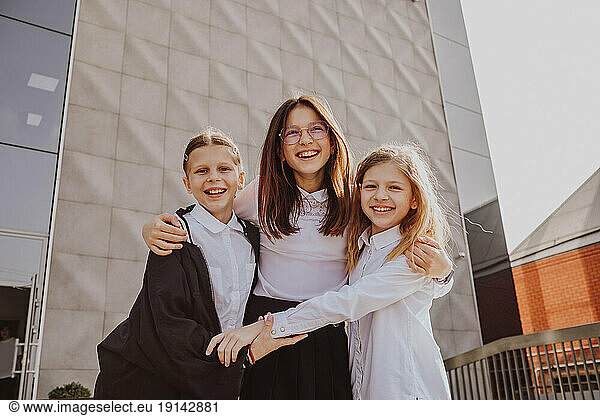 Happy girl with arm around friends standing in front of school building
