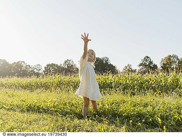 Happy girl with arm raised standing in meadow on a sunny day