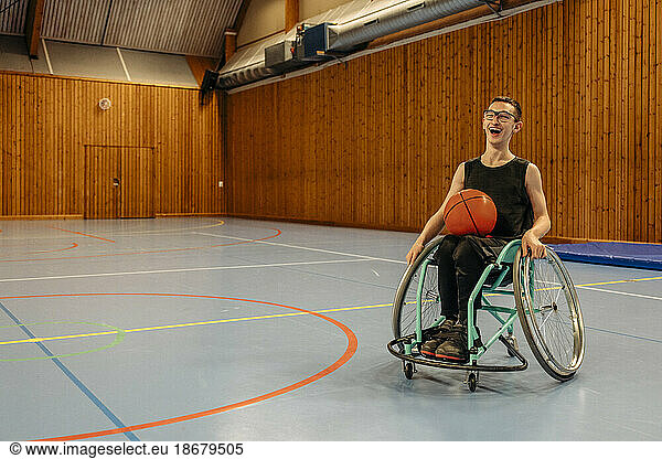 Happy girl with basketball sitting on wheelchair at sports court