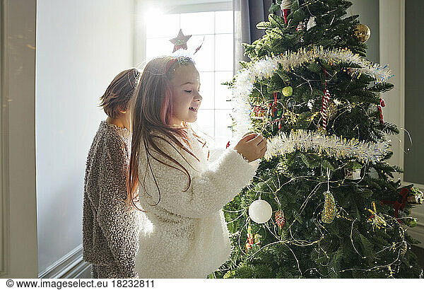 Happy girl with brother decorating Christmas tree in bedroom at home