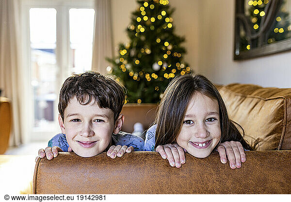 Happy girl with brother having fun on sofa at home at Christmas time