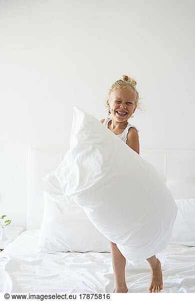 Happy girl with pillow having fun on bed