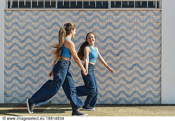 Happy girls holding hands and running in front of wall