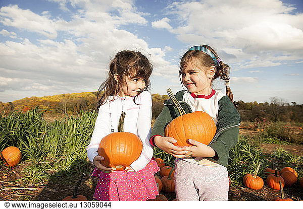 Happy girls holding pumpkins and looking face to face