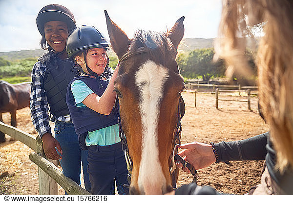 Happy girls learning horseback riding in sunny paddock