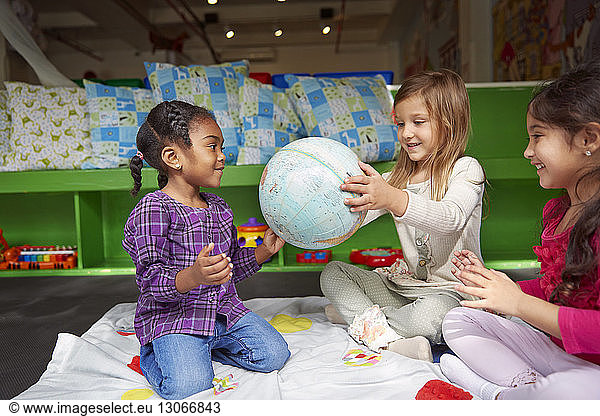 Happy girls playing with globe on blanket at child care