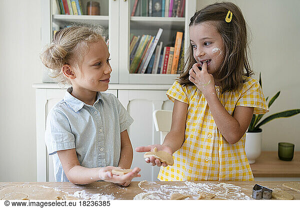 Happy girls preparing cookies with dough on table at home
