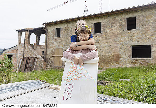 Happy girls standing with drawing in front of house