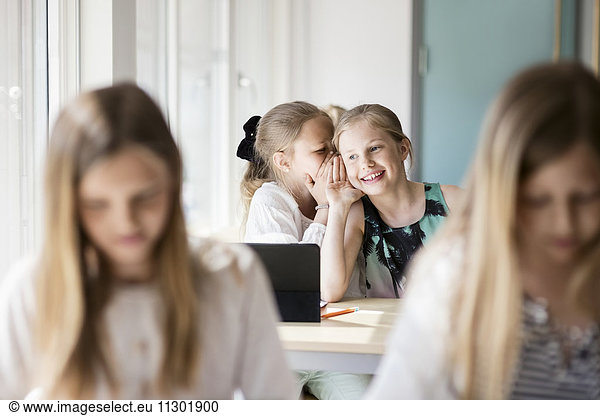 Happy girls whispering in classroom