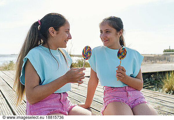 Happy girls with lollipops sitting on boardwalk