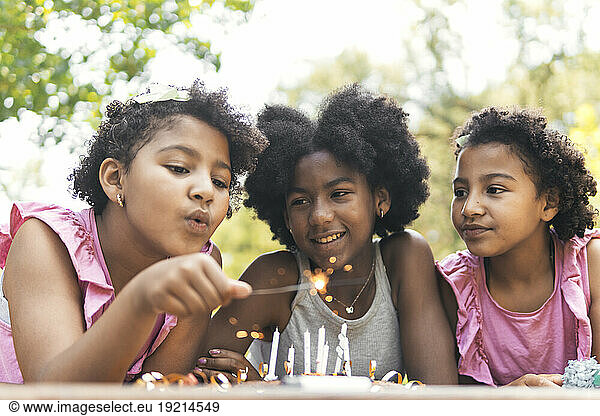 Happy girls with sister blowing birthday candles in garden