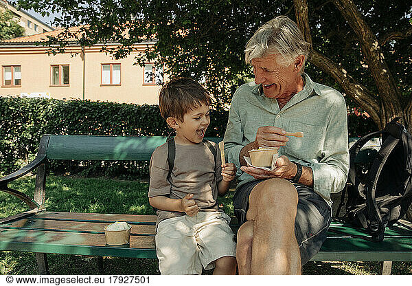 Happy grandfather and grandson enjoying ice cream while sitting on bench