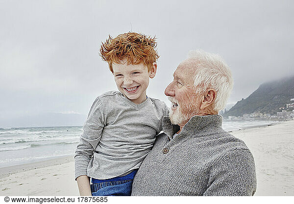 Happy grandfather carrying his grandson at the sea
