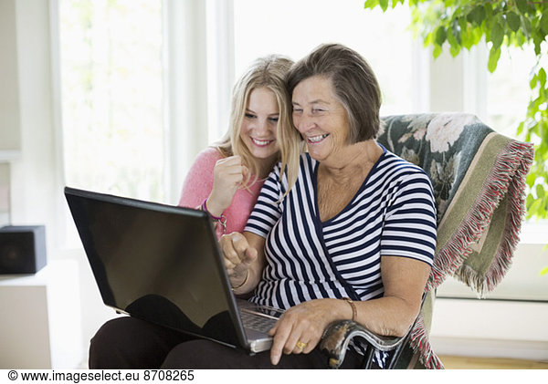 Happy grandmother and granddaughter using laptop at home