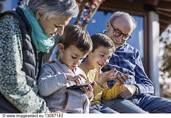 Happy grandparents and grandsons using smart phones in park