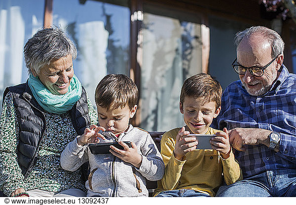 Happy grandparents looking at grandsons using smart phones in park