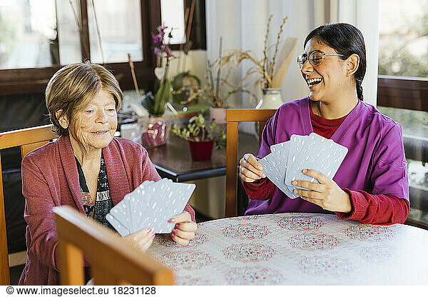 Happy healthcare worker playing cards with senior woman at home
