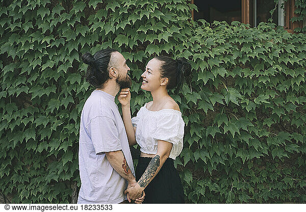 Happy hipster couple holding hands standing by green ivy plants